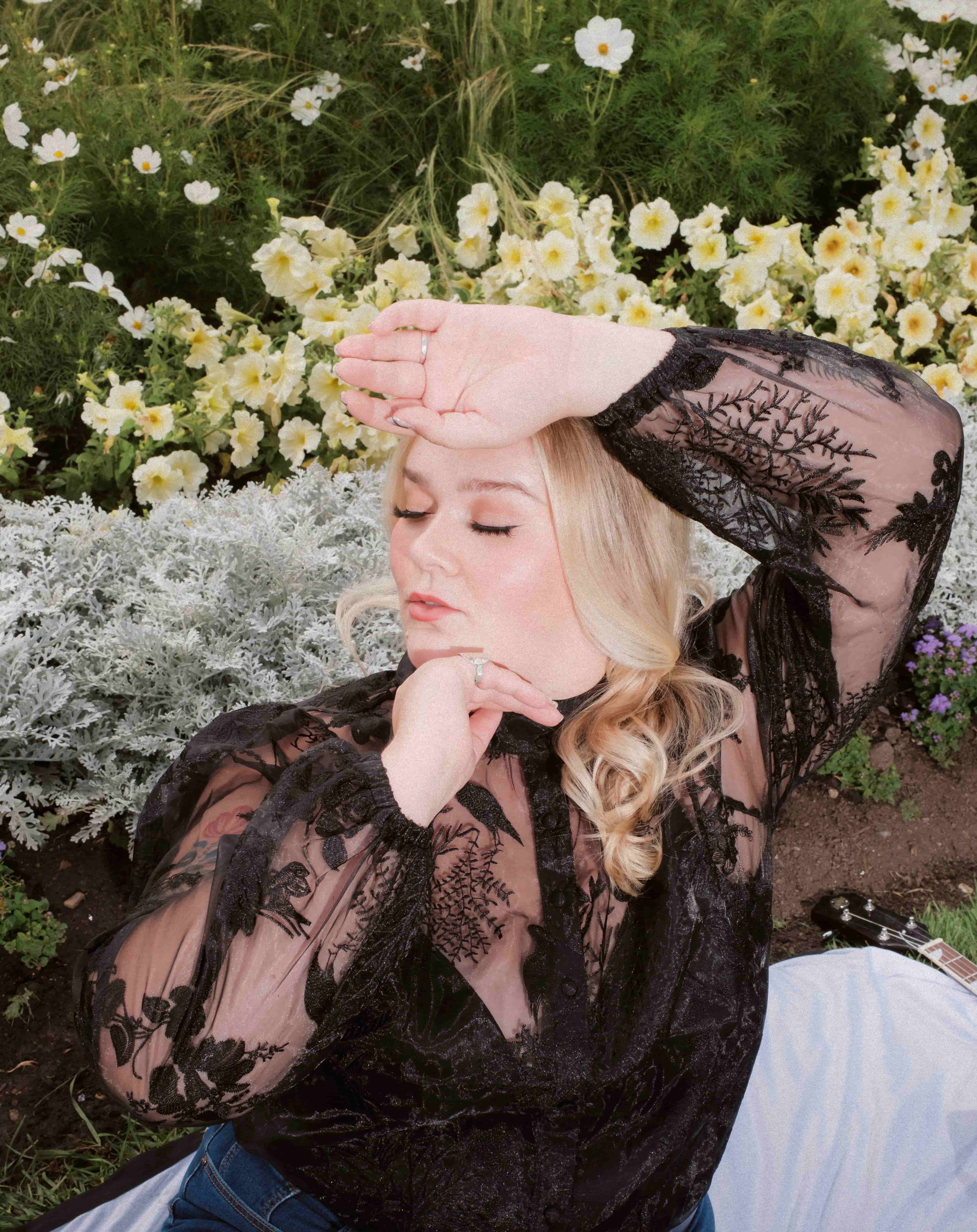 blond woman posing in a natural and bright environment. She is wearing a mesh dark top