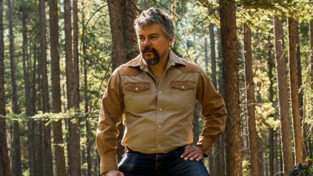 Artist Brian Jungen looking into the distance surrounded by a forest. 