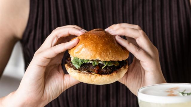 Person holding hamburger with fries and cocktail
