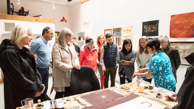 Guests gather around a table as a visual artists displays her work. 