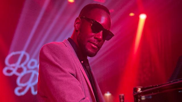 Timothonius wearing sunglasses playing the piano in dark club