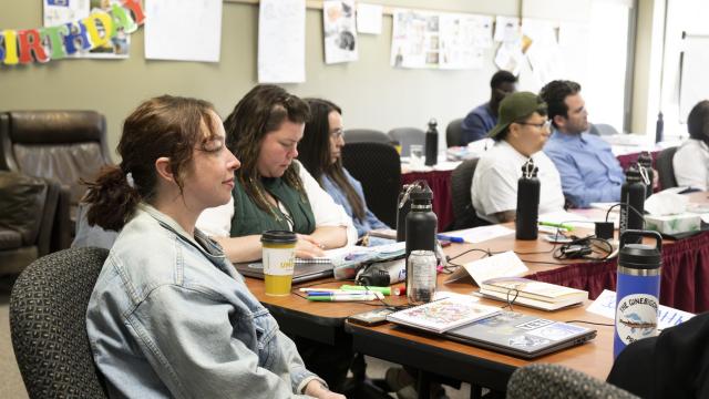A group of people are seated in a conference room listening to a presentation