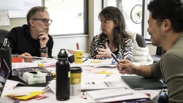 Three people are seated at a table having a discussion