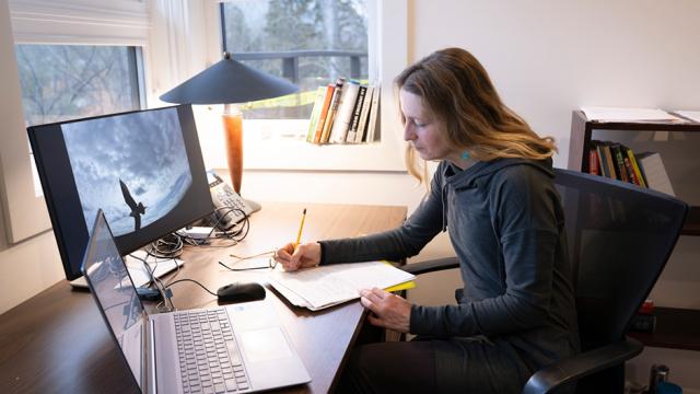 A writer is working at a desk in front of a window