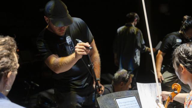 An audio engineer participant adjusts a microphone for a musician holding a violin