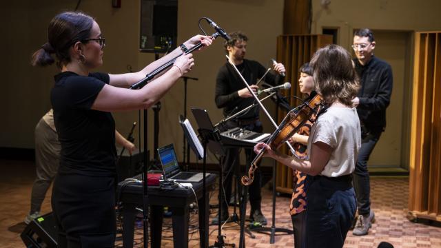 An audio engineer participant adjusts a microphone for a musician holding a violin