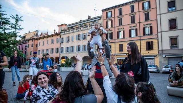 A group of smiling people are crowded around a baby who is being held up in the air