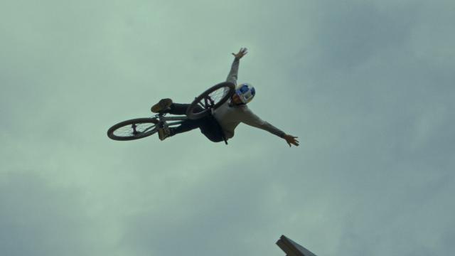 A fearless mann wearing a helmet taking a jump on his bike, spreading his arms like wings