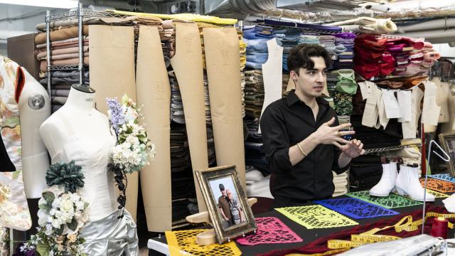 A wardrobe technician is standing in a studio filled with fabrics and costumes