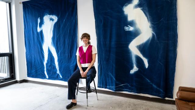 An artist is sitting in front of two large tapestries