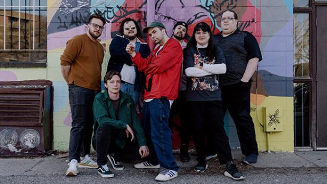 Midnight channel collective standing against a graffitied wall. 