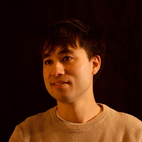 Man with slight smile staring off camera against a black background