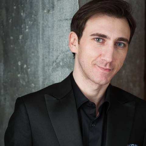 Man leaning against wall in dark suit smiling at camera