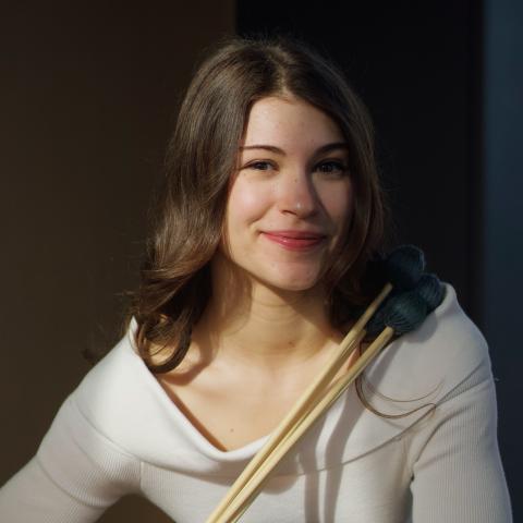 Woman holding drum sticks in front of her while smiling at camera
