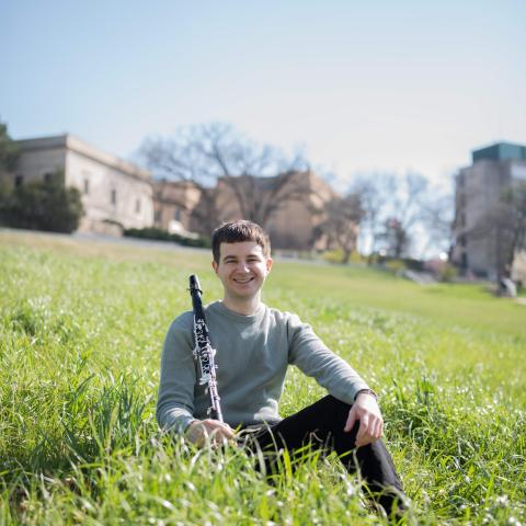 Clarinetist sitting in long grass in a field in front of houses