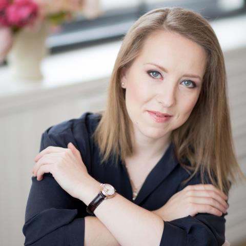Woman sitting backwards on a chair smiling at the camera with arms crossed over shoulders