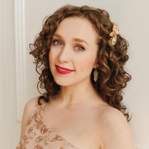 Woman with long brown curly hair smiling lightly at camera