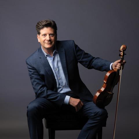 Barry Shiffman is seated on a chair with a violin resting on his knee.