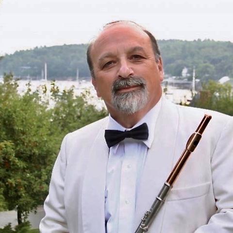 Thomas Wolf is wearing a white jacket, black bowtie, and holding a flute