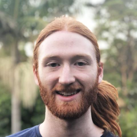 Man with long pulled back hair in a blue t-shirt smiling at the camera