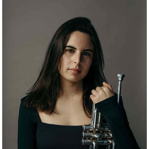 Woman posing by holding trumpet upright resting against her body