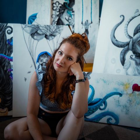 Angel Everett sits in front of a collection of her large-scale paintings, a paintbrush tucked into her hair.