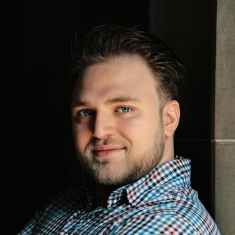 Man in plaid shirt arms crossed leaning against wall