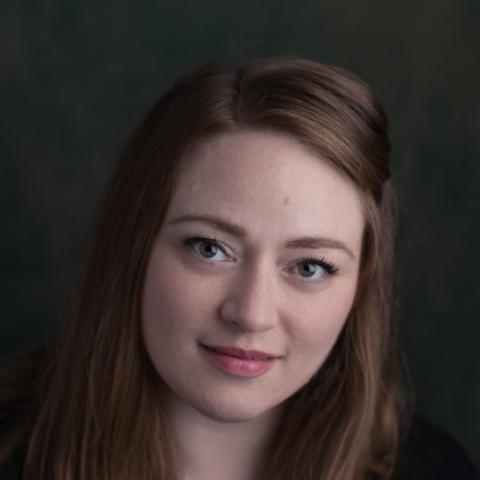 Woman with red hair flowing over shoulders smiling lightly and directly at camera