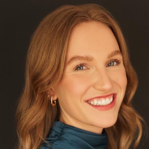 Woman smiling broadly at camera with flowing red hair and a teal halter dress