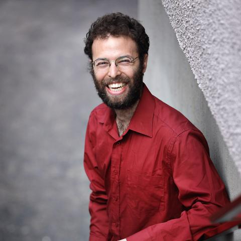 Man standing in a stairwell wearing a red shirt smiling directly at camera