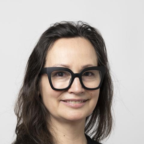 Woman with long hair and thick black glasses smiling directly at camera