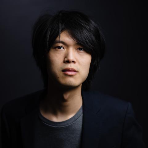 Man staring directly at camera in dark suit and dark room