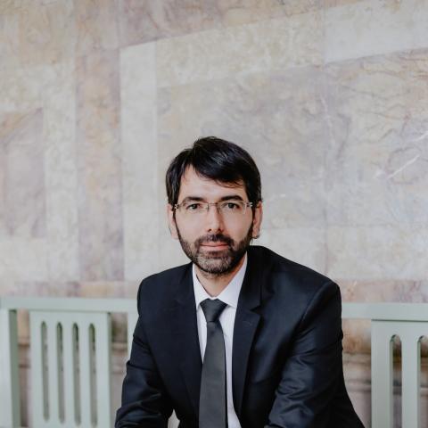 Man sitting on a bench in a suit with hands clasped in front of him