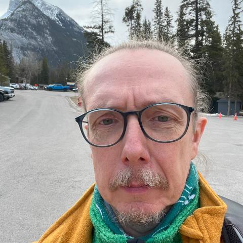 Man with glasses and pulled back hair standing in front of Rundle Mountain