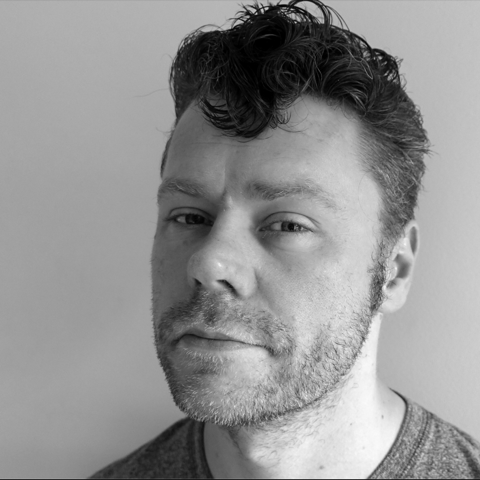 Man with short curly hair smiling slightly at the camera in black and white image