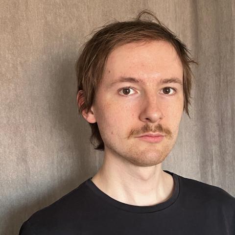 Man in black t-shirt standing against wall and looking at camera