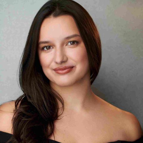 Woman with long black hair flowing over one shoulder smiling at camera in off the shoulder black dress