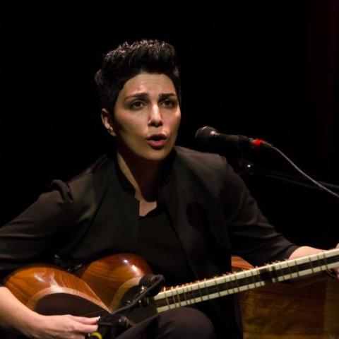 A woman with short hair in dark clothing playing a stringed instrument