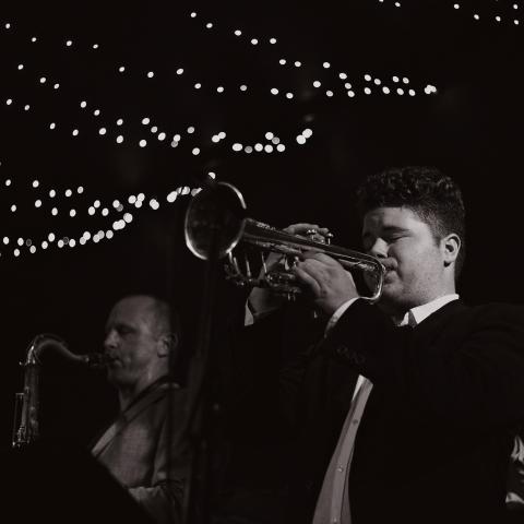 Photo taken at night with man playing trumpet under string of lights