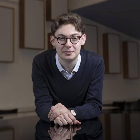 Man with glasses in black sweater and white collared shirt looking at camera