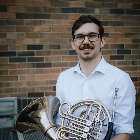 Man smiling at camera holding french horn on lap