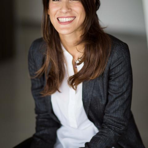 Woman in casual business attire with long hair and a large smile staring directly at camera