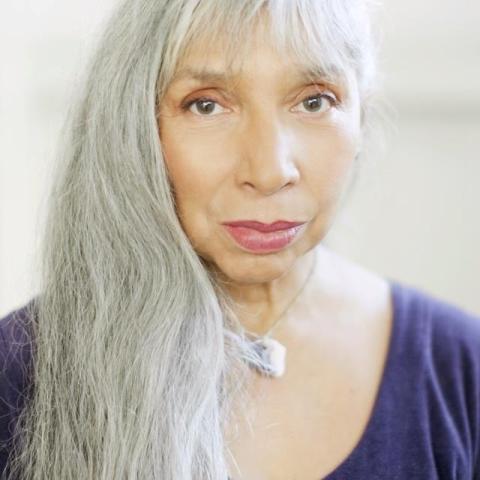 Monique wearing a blue shirt with silver hair on her shoulder looking directly at the camera