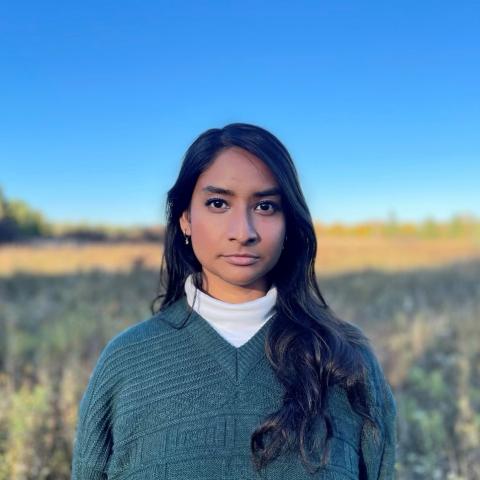 Woman standing in a field in a green sweater and white turtleneck staring directly at the camera