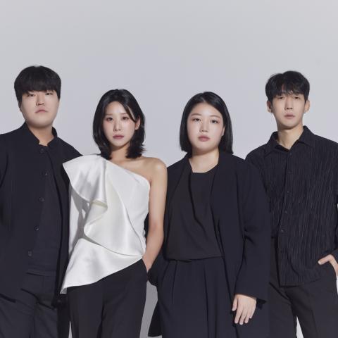 Quartet members all dressed in black except for violinist in white dress top against a grey wall
