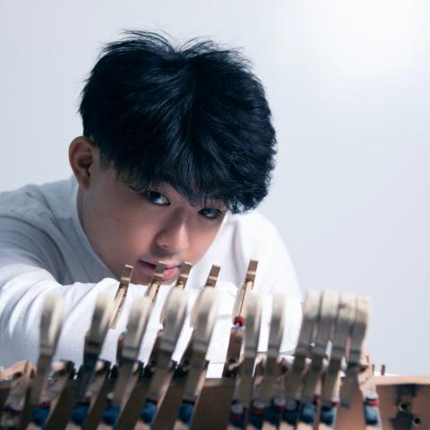 Short haired man in white shirt leaning his chin on his arm behind piano keys