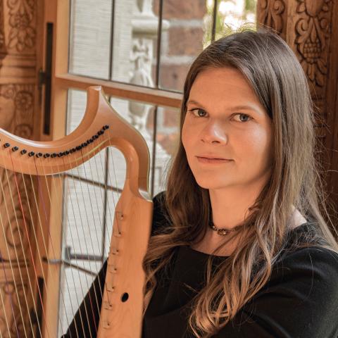 Woman sitting at a harp and smiling slightly at the camera