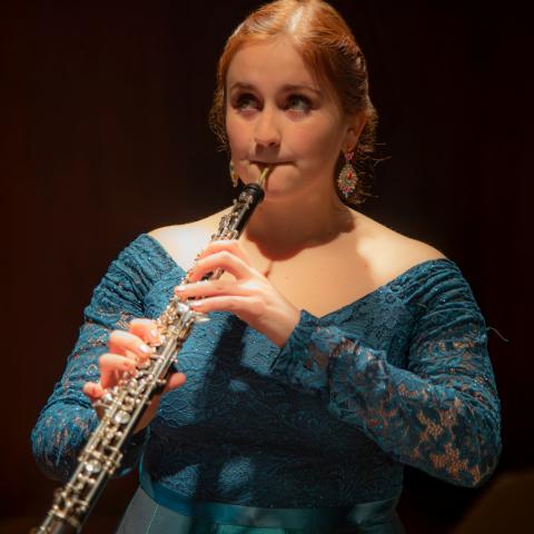 Woman playing the oboe in concert in a green formal dress