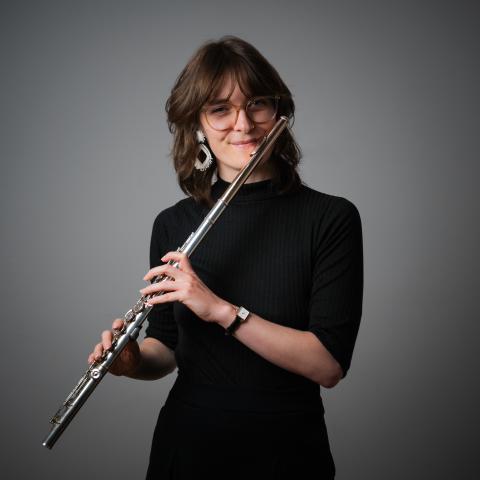 Woman in a black dress holding the flute to her mouth and smiling at the camera 