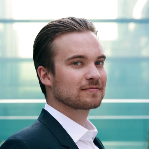 Man with light, short hair smiling at the camera in a dark suit jacket and white dress shirt